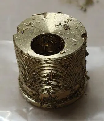 Threaded brass plug as machined — fine swarf bound to every thread and face by cutting oil.