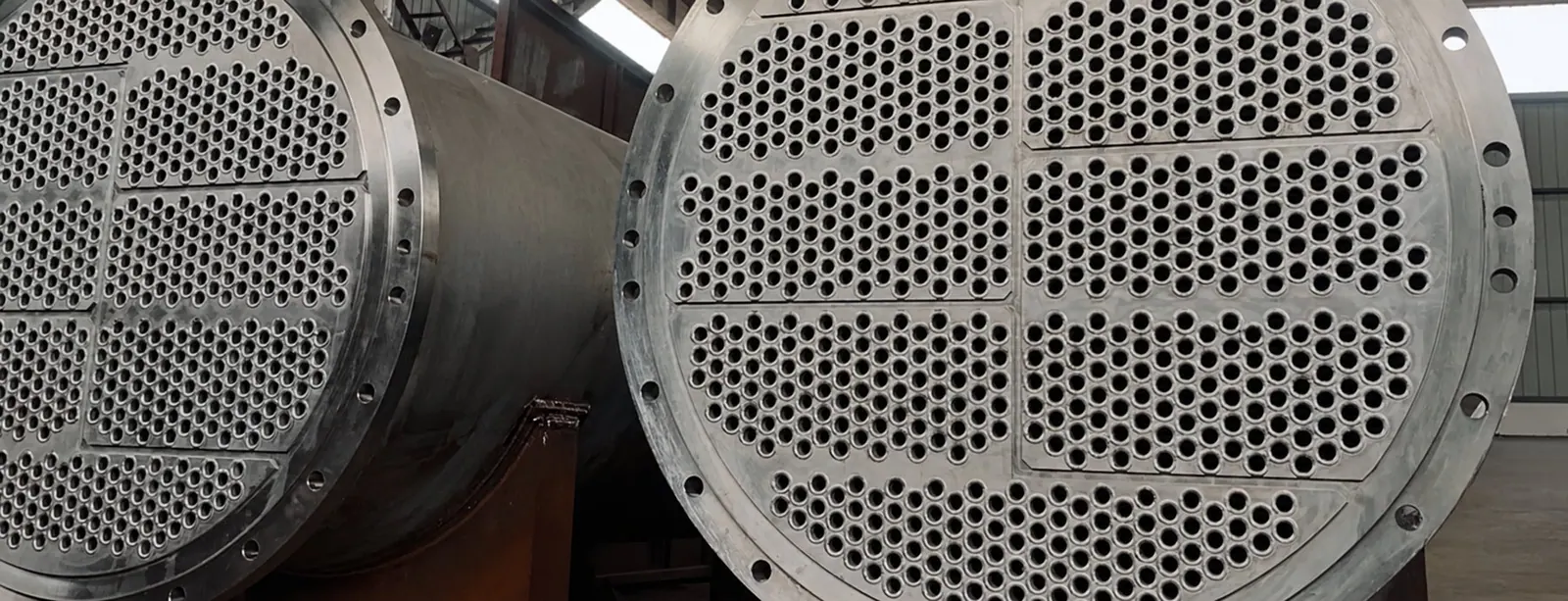 Two shell-and-tube heat exchanger bundles on a workshop floor, tube sheets and flanges facing the camera